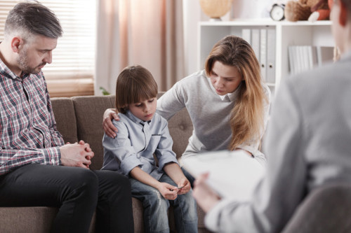 3 köpfige Familie sitzt bei einer Familienberatung in Stuttgart, Kind schaut traurig