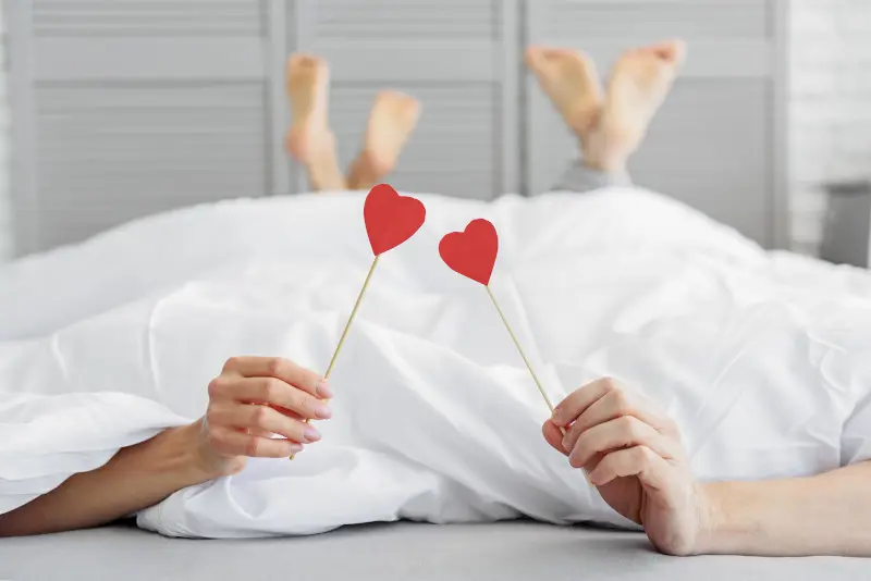 Ein Paar liegt unter einer Decke, Stäbe mit Herzen drauf in der Hand